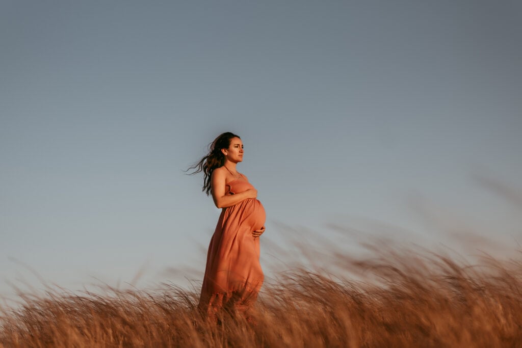 Maternity Photographer, an expectant pregnant mother stands before a blue sky in tall dry grass