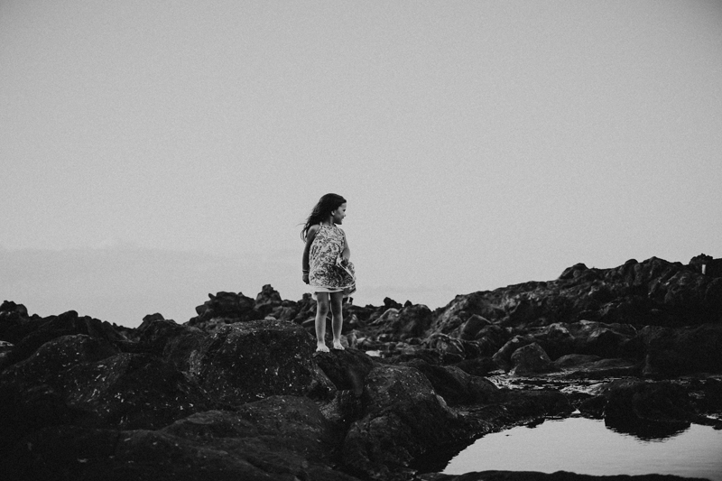 Family Photographer, a little girl stands on rocks near the ocean